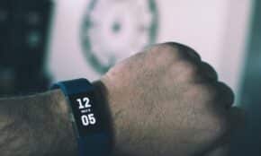 Close-up of a digital smartwatch showing time and date on a man's wrist indoors.