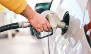 Close-up of a person refueling a car with a gas nozzle at a station.
