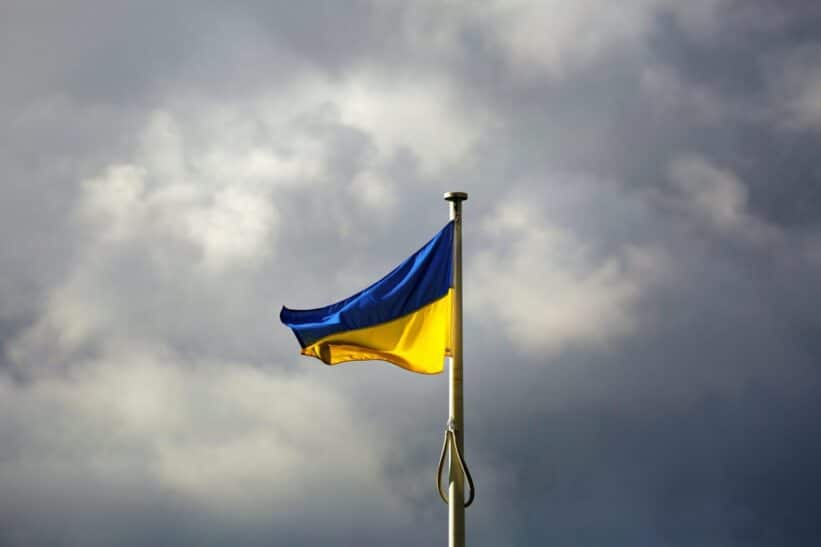 A Ukrainian flag waves prominently against a dramatic cloudy sky, symbolizing resilience.
