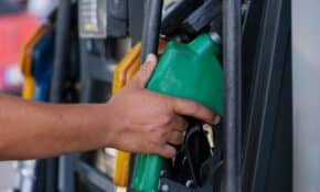 Close-up of a hand holding a green fuel nozzle at a gas pump station outdoors.