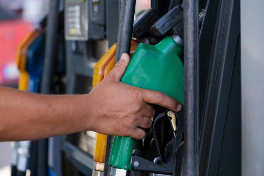 Close-up of a hand holding a green fuel nozzle at a gas pump station outdoors.
