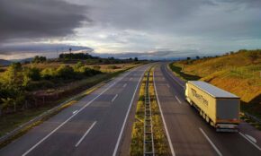 A scenic highway under a dramatic cloudy sky with a lone truck driving on an open road.