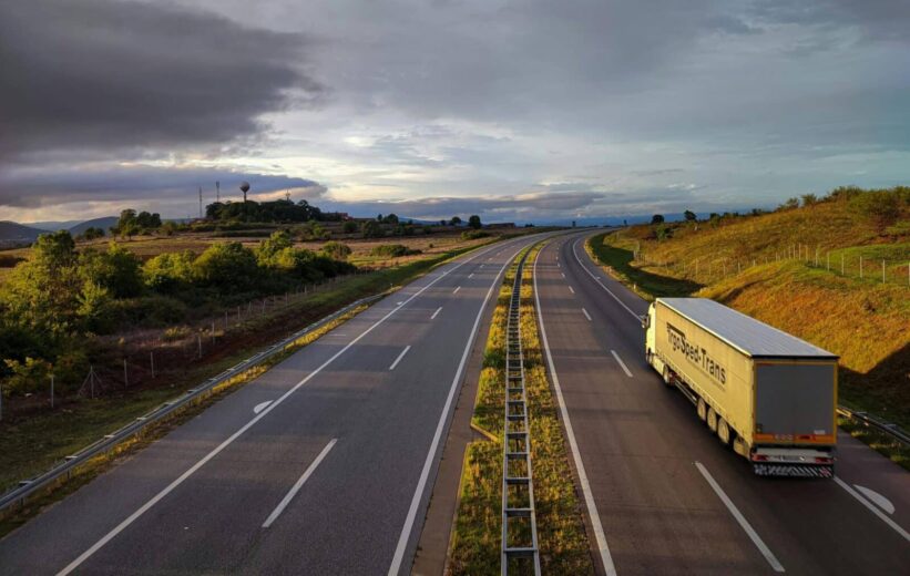 A scenic highway under a dramatic cloudy sky with a lone truck driving on an open road.
