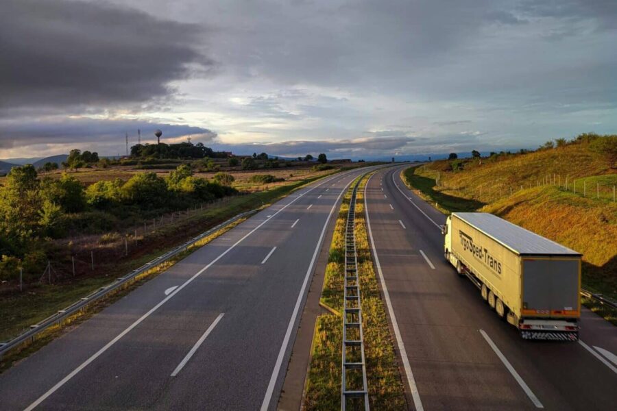 A scenic highway under a dramatic cloudy sky with a lone truck driving on an open road.