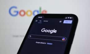 Smartphone screen showing Google search in dark mode with the Google logo in the background.