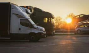 A row of trucks and car transporter parked at sunset in an open parking lot, highlighting the golden hour.