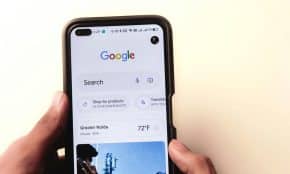 A close-up of a hand holding a smartphone with Google search displayed on the screen.