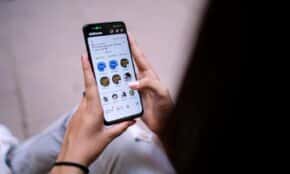 Close-up of a woman using a smartphone with social media app open. Hands holding device.