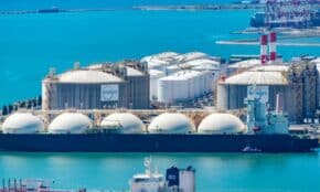 Aerial shot of a gas terminal featuring LNG storage tanks and tanker ships in turquoise waters.