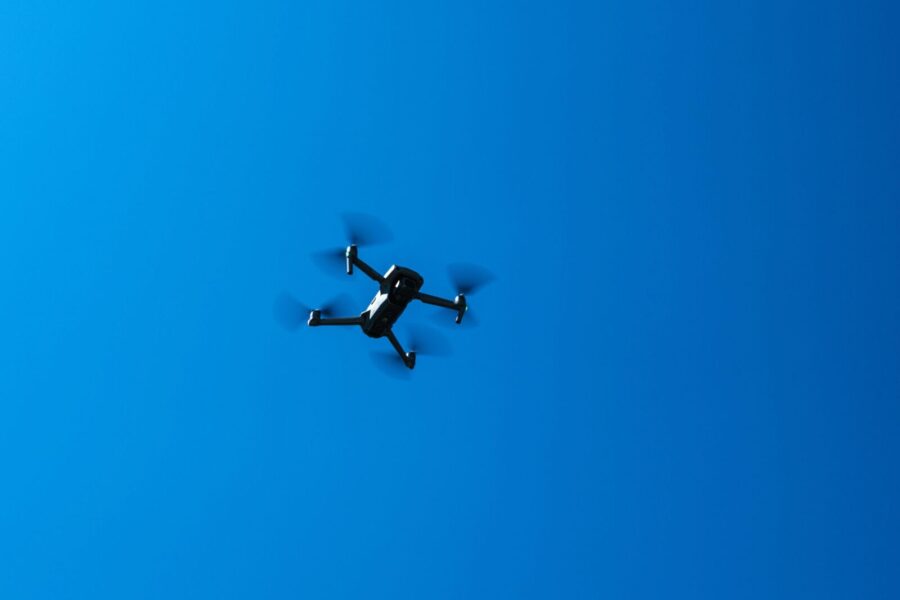 A black drone flying high in a clear blue sky, showcasing modern technology and flight capabilities.