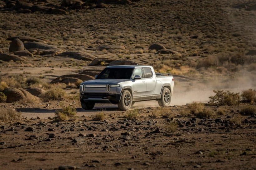 Electric pickup truck navigating a rocky desert landscape, showcasing off-road capability and rugged terrain.