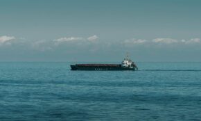 A cargo ship cruising through calm ocean waters under a clear sky.