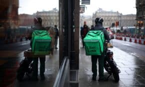 Uber Eats courier on motorbike in Edinburgh with mirror reflection on rainy street day.