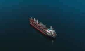 An aerial shot of a cargo ship navigating the open sea, surrounded by deep blue water.