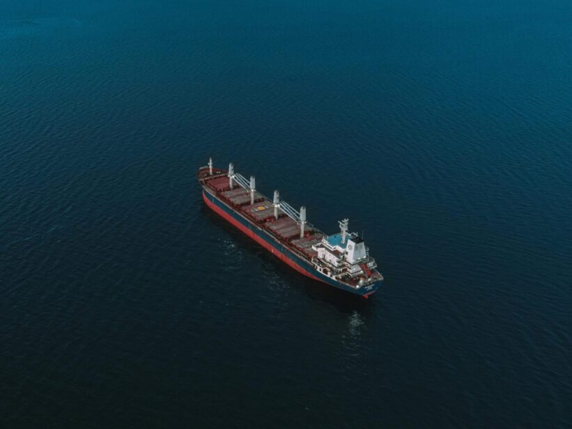 An aerial shot of a cargo ship navigating the open sea, surrounded by deep blue water.