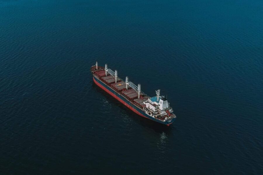 An aerial shot of a cargo ship navigating the open sea, surrounded by deep blue water.