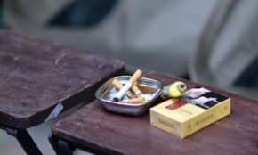 Close-up of ashtray with cigarette butts and a pack of cigarettes on a rustic wooden table.