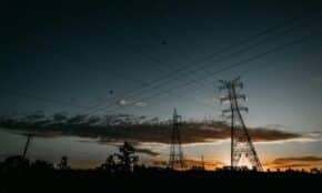 Electricity towers silhouetted against a vibrant sunset sky with power lines stretching across.