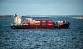 A large container ship transports cargo across the open sea under a clear sky. Ideal for shipping and logistics themes.