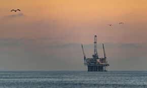 Oil platform silhouetted against a vibrant sunset in Huntington Beach, California.