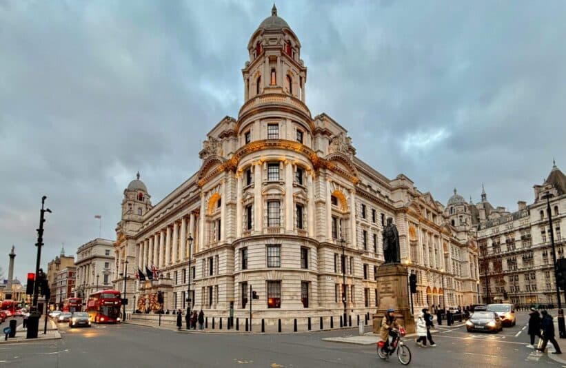 A bustling street scene featuring a grand Edwardian building in Central London at dusk, showcasing urban life.