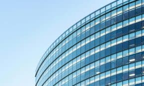 Low angle view of a modern glass office building against a clear blue sky.