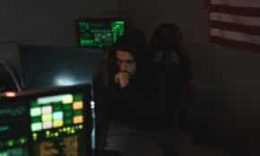 A cybersecurity expert monitors multiple screens, focused on data protection in a dark room.