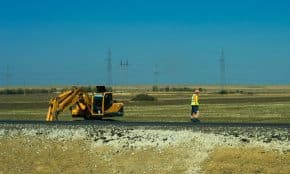 Man working on a road construction site with an excavator outdoors.