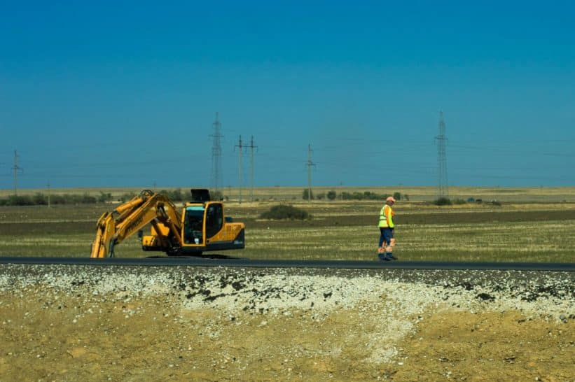 Man working on a road construction site with an excavator outdoors.