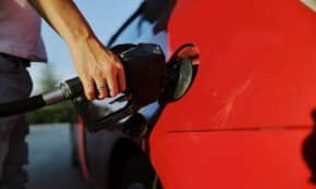 Close-up of a person refueling a red car at an outdoor gas station during the day.