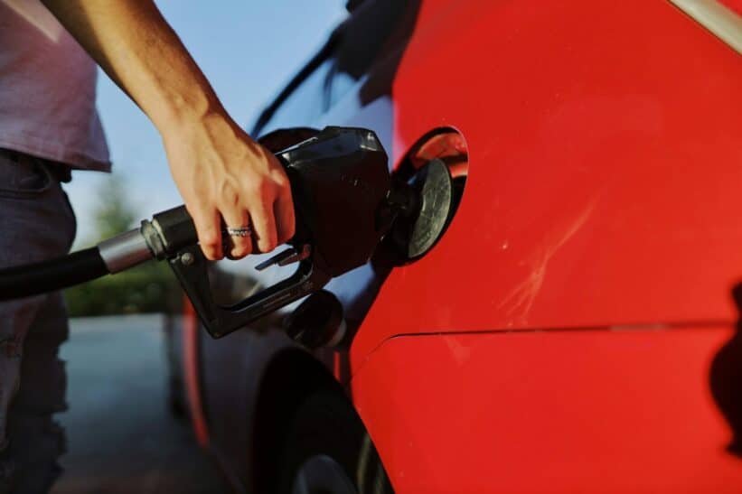 Close-up of a person refueling a red car at an outdoor gas station during the day.