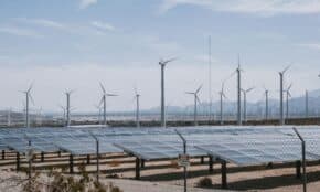 A renewable energy farm with wind turbines and solar panels under a clear sky.