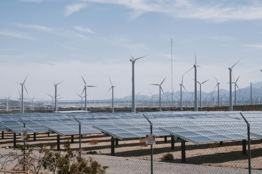 A renewable energy farm with wind turbines and solar panels under a clear sky.