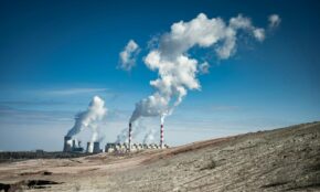 Industrial power plant emitting smoke under a clear blue sky.