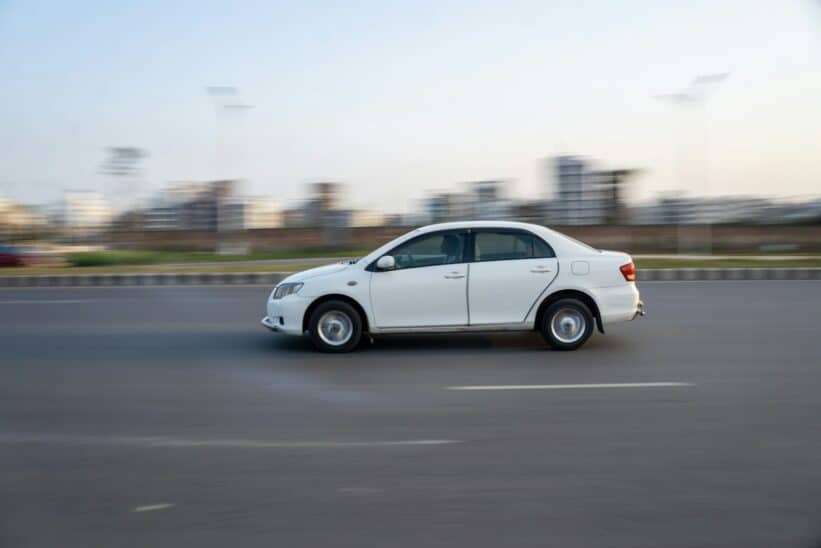 A white car speeds down a road.