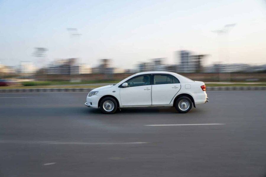 A white car speeds down a road.
