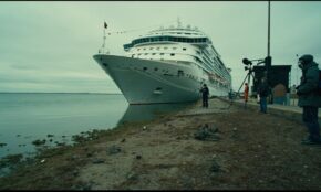Cruise ship docked in Argentina with passengers disembarking as news crews film, marshy area with rodents visible nearby