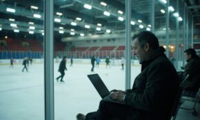 Professional man using half-open laptop while watching ice skating practice, demonstrating modern AI-powered work habits